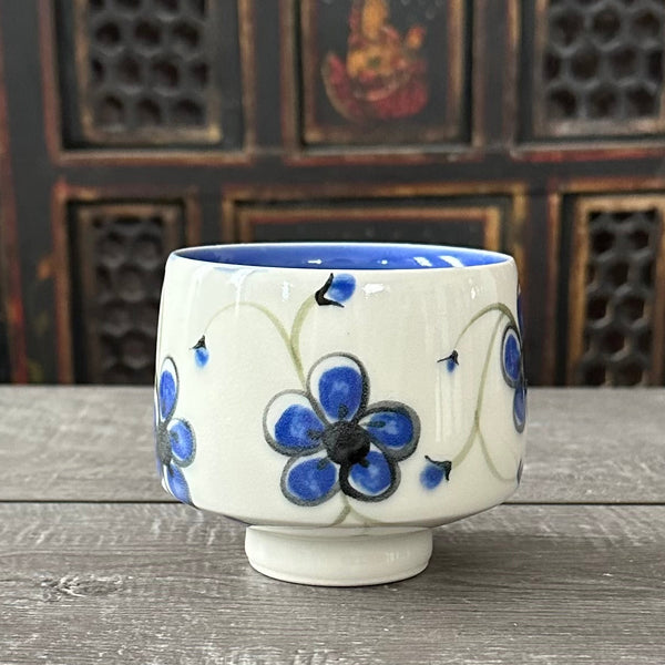Porcelain tea bowl with blue plumflower design on a white porcelain surface, blue glaze inside and clear glaze outside